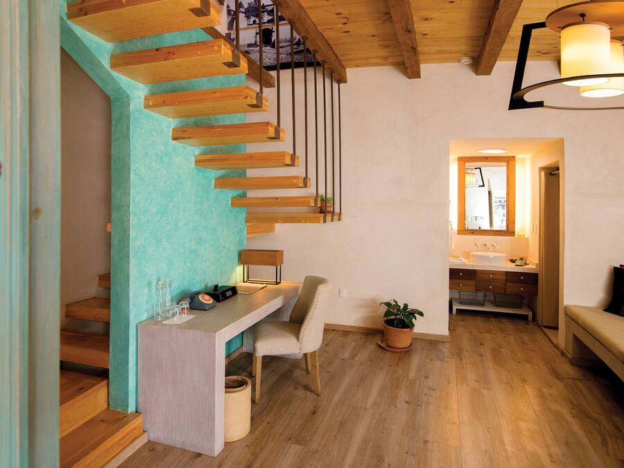 Un interior moderno con una escalera de madera, un escritorio con una silla, una planta en maceta y un banco.