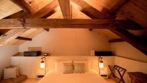 Un dormitorio acogedor en el ático, con techo de madera, una cama con ropa de cama a rayas, dos lámparas de noche y una pequeña silla de madera.