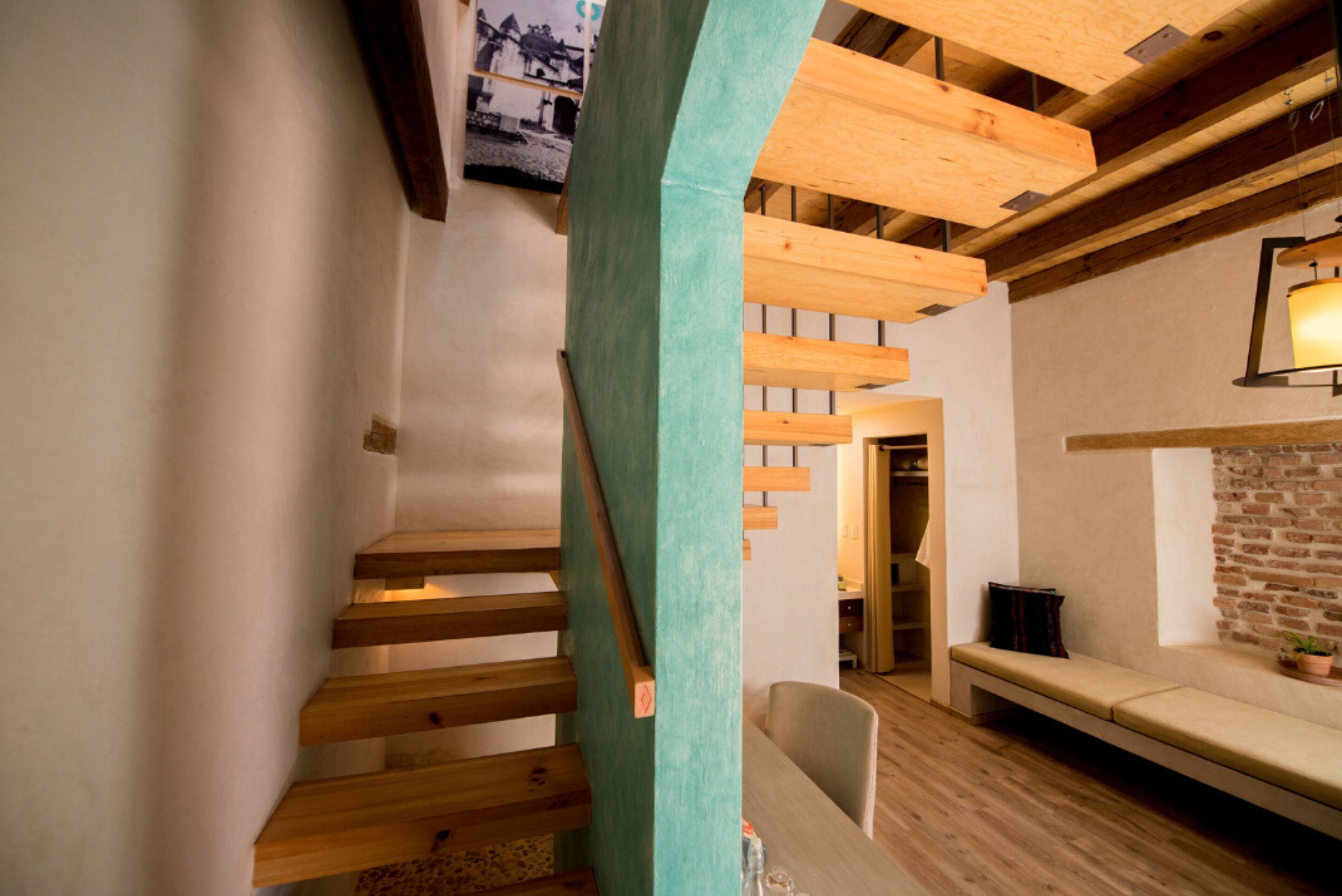 A wooden staircase leading to a loft area with a bench and a brick wall.