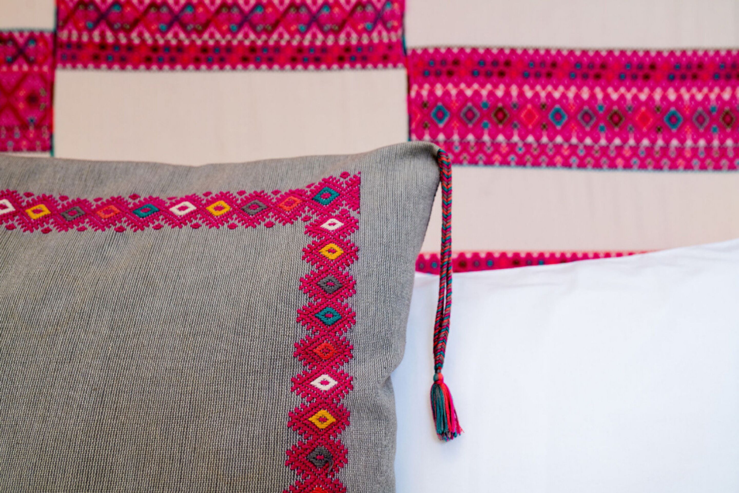 A bed with a grey blanket and a colorful embroidered border.