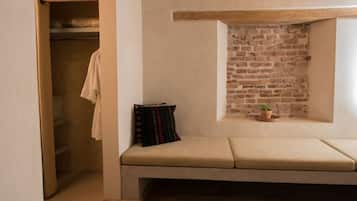A room with a built-in bench, a small window with a brick wall, and a closet with a hanging towel.