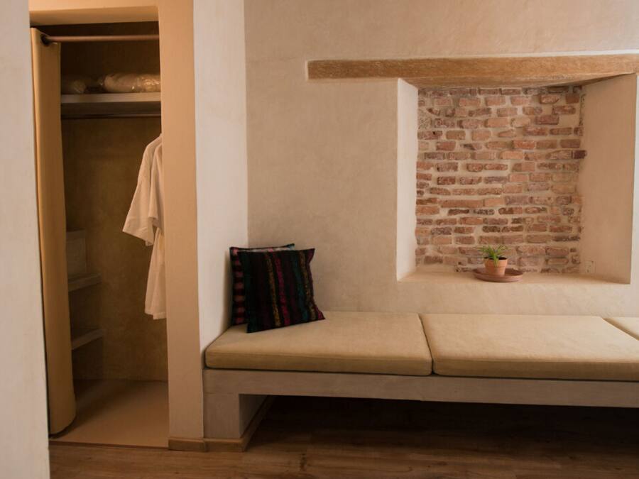 A room with a built-in bench, a small window with a brick wall, and a closet with a hanging towel.