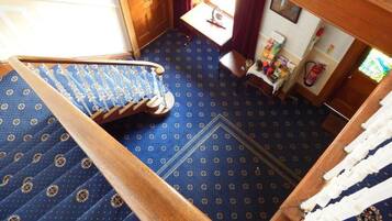 A room with a patterned carpet, a wooden staircase, a small table with items, and a window with curtains.