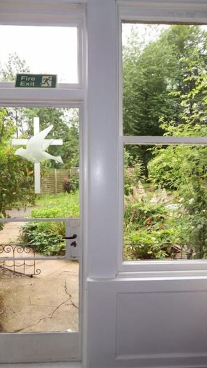 A white door with a window, a fire exit sign, and a garden view. - Whitchester Christian Guest House (Hawick)