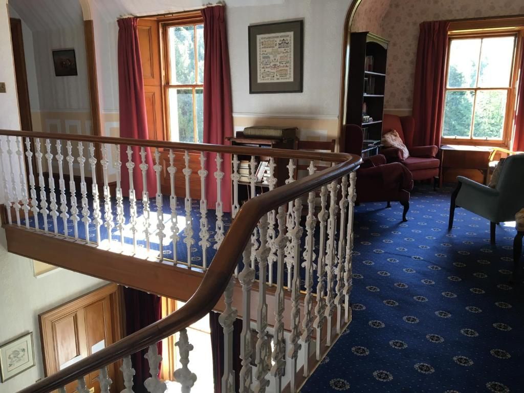 Um quarto com carpete azul estampado, escada de madeira com balaústres brancos e uma cadeira vermelha.