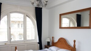 Un dormitorio con un amplio ventanal de arco, una cama de madera, una mesita de noche con una lámpara y un espejo en la pared.