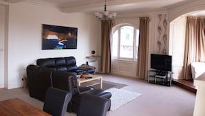 Una sala de estar con un sofá de cuero negro, una mesa de centro, un televisor sobre un mueble bajo y un cuadro en la pared.