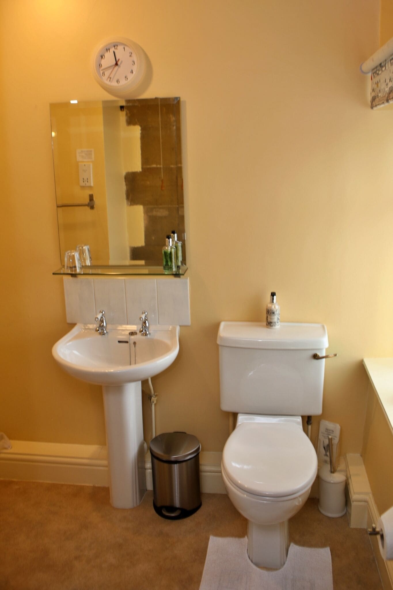 A bathroom with a sink, toilet, and a clock on the wall.