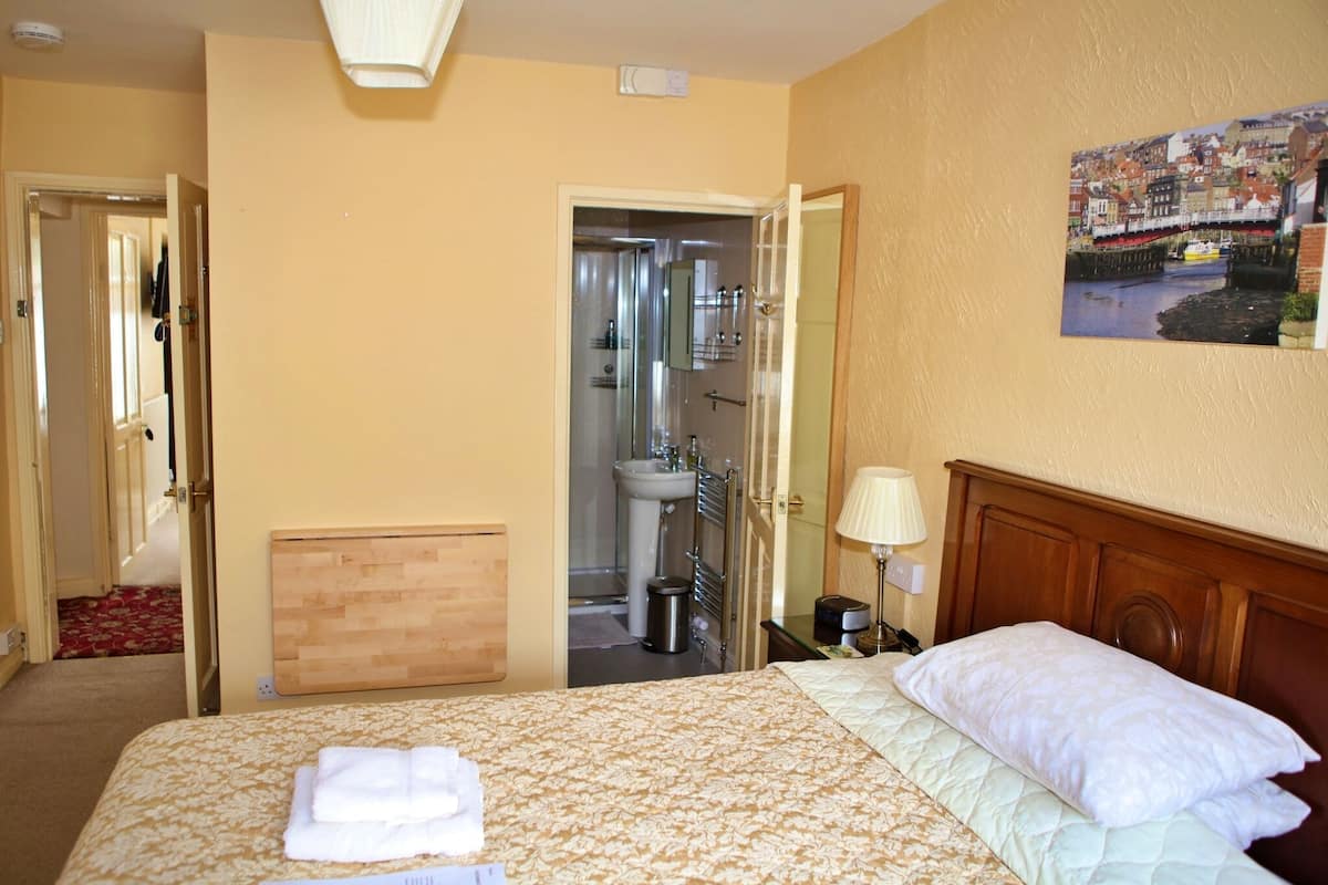 A hotel room with a bed, a bathroom visible through an open door, and a cityscape painting on the wall.