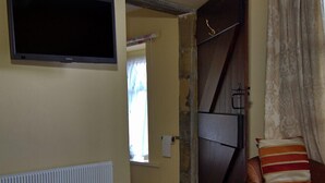 A hotel room with a bed, a TV mounted on the wall, a window with curtains, and a door. - Wortley Cottage Guest House (Sheffield)