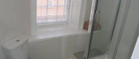 Et badeværelse med toilet, et vindue og en brusekabine i glas.