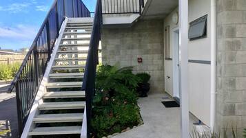 A staircase leading to a building with a fire alarm on the wall, a door, and a small garden area with plants and flowers.