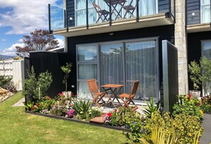 Un edificio moderno de dos plantas con balcón, mobiliario exterior y un jardín bien cuidado.
