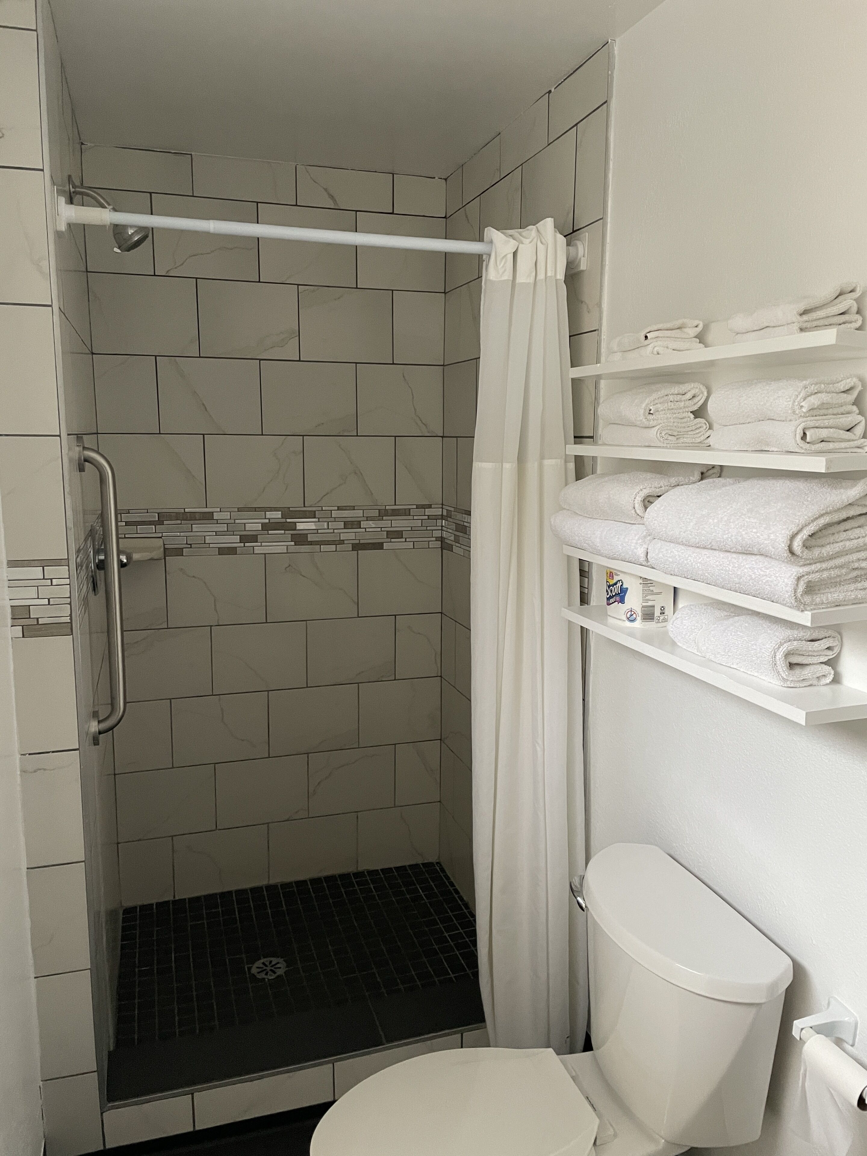 Une salle de bain avec une douche, des toilettes et des étagères où sont pliées les serviettes.