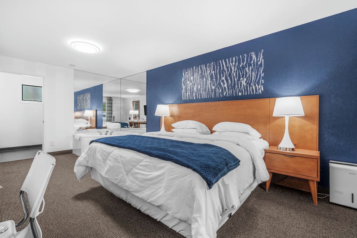 Une chambre d’hôtel avec un grand lit, deux tables de chevet avec des lampes, un mur bleu à motifs et un petit radiateur.