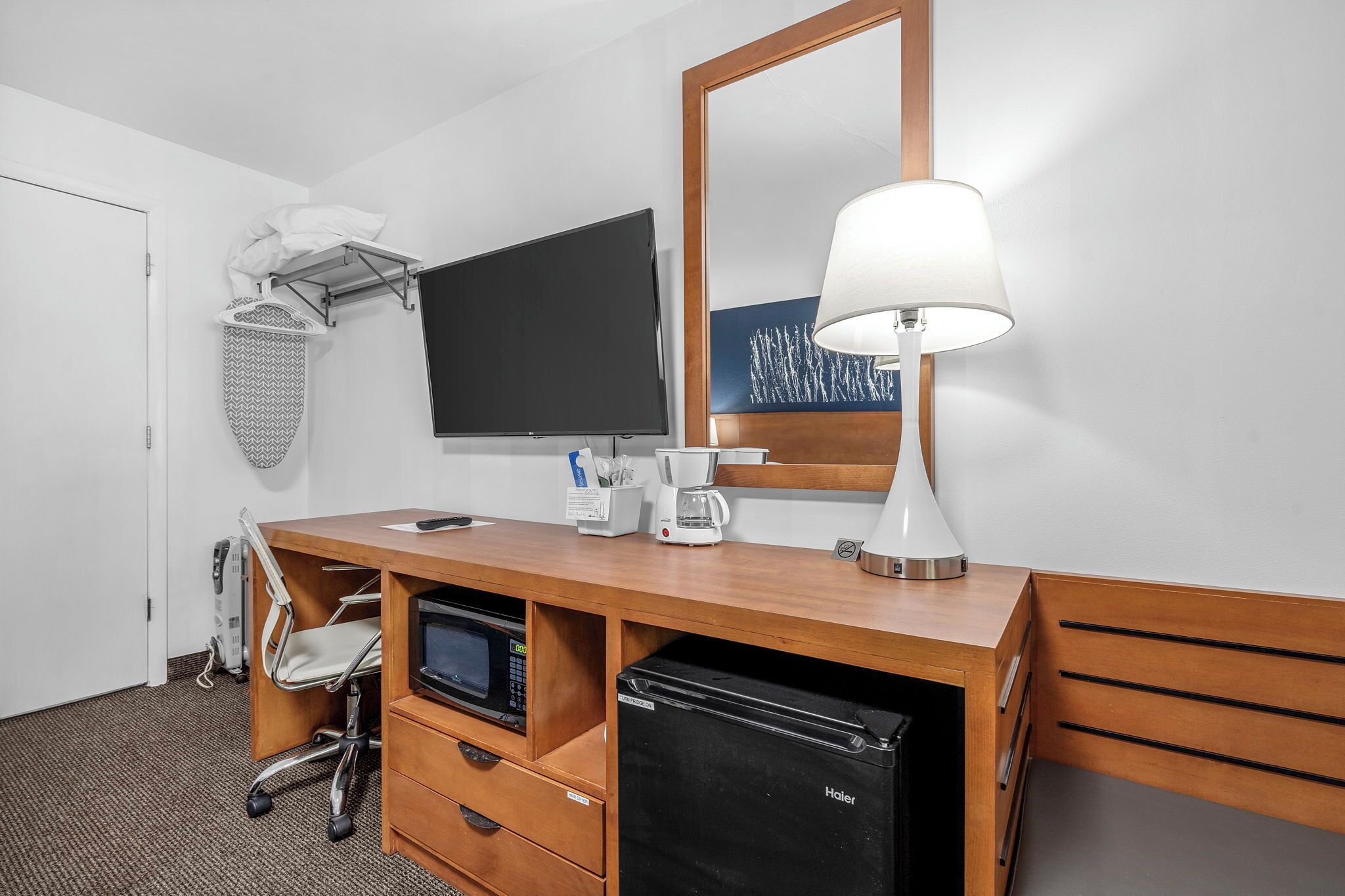 Een hotelkamer met een houten bureau, een flatscreen televisie, een lamp, een koffiezetapparaat, een magnetron en een minibar.