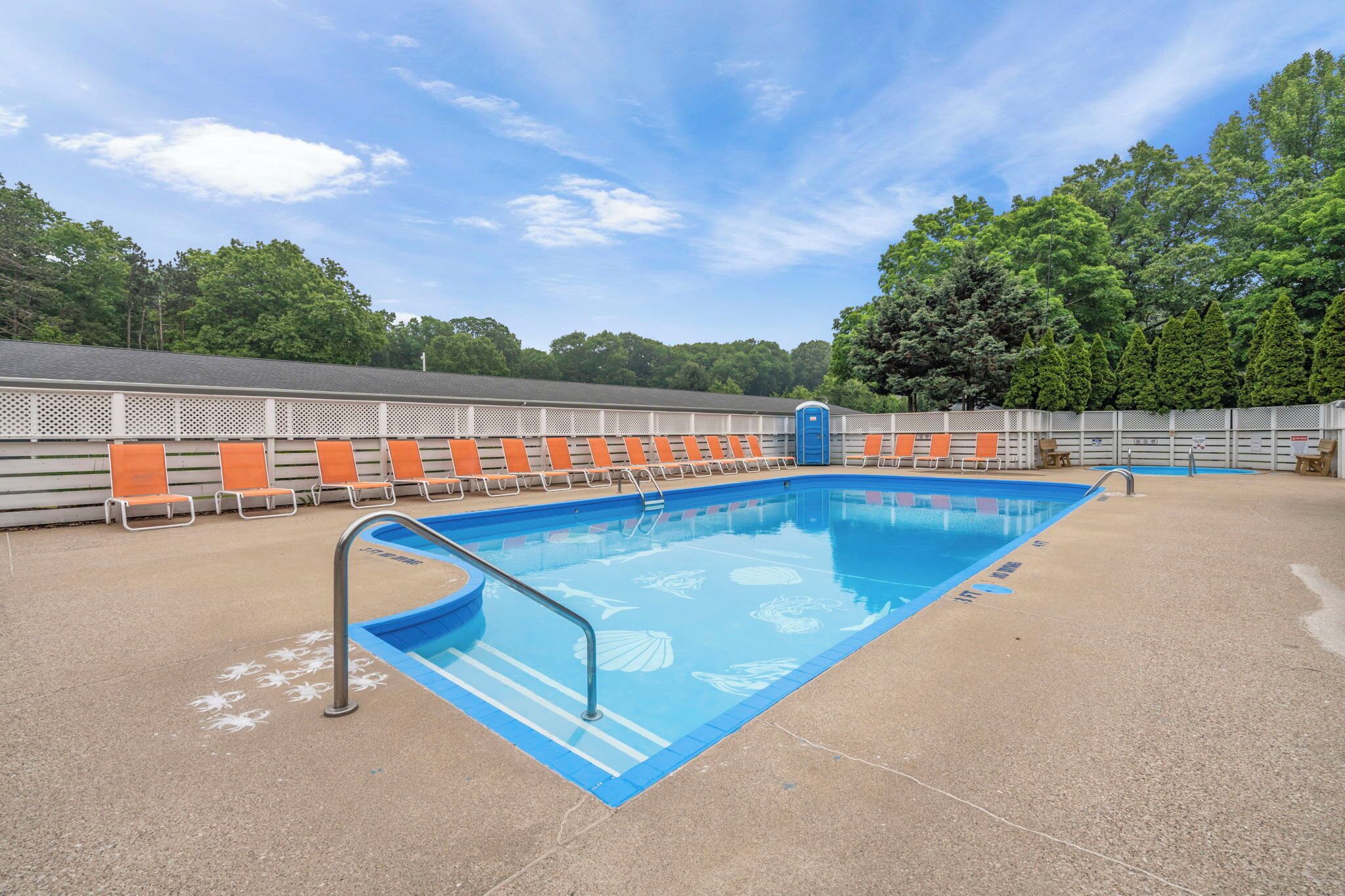 Une piscine aux carreaux bleus et une échelle en métal, entourée de chaises longues orange et blanches.