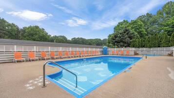 A swimming pool with blue tiles and a metal ladder, surrounded by orange and white lounge chairs.