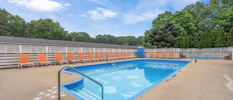 Une piscine aux carreaux bleus et une échelle en métal, entourée de chaises longues orange et blanches.