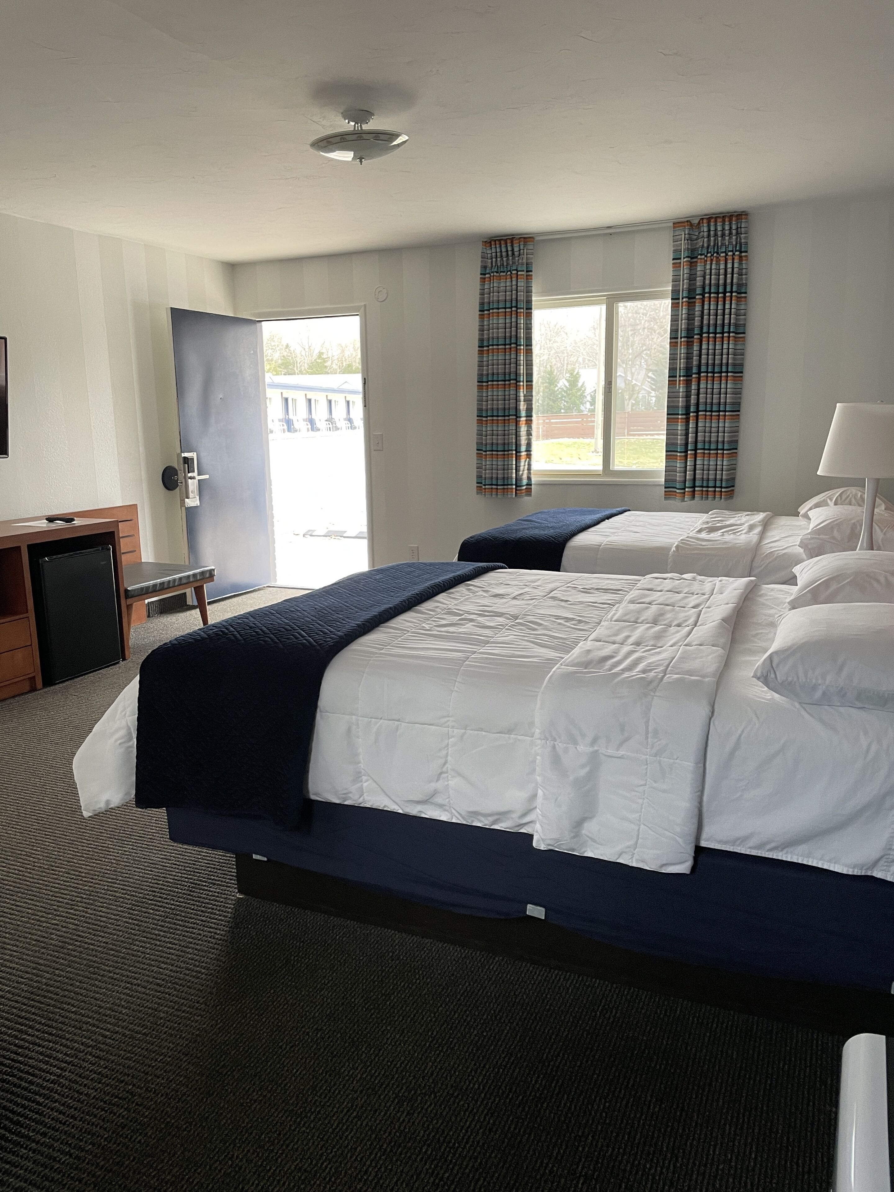Habitación de hotel con dos camas, un escritorio y una puerta que da a un balcón.