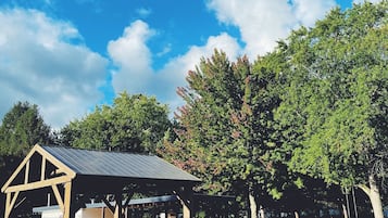 A covered picnic area with tables and chairs, surrounded by trees and a clear blue sky.