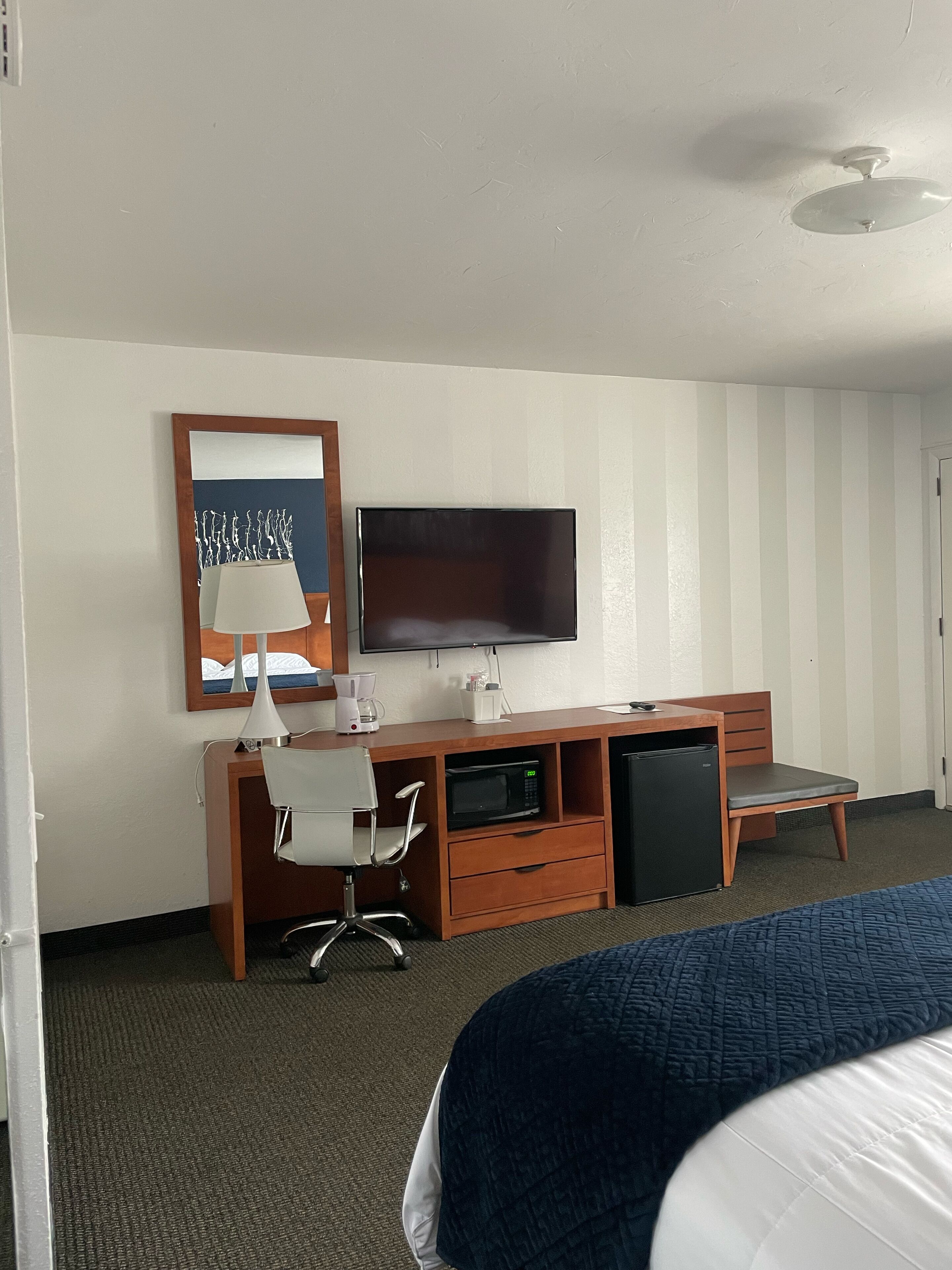 Quarto de hotel com cama, escrivaninha com cadeira, televisão e micro-ondas.