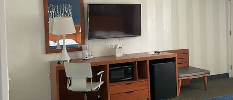 Quarto de hotel com cama, escrivaninha com cadeira, televisão e micro-ondas.