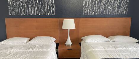 A hotel room with two beds, a wooden headboard, a nightstand with a lamp, and a textured wall decoration.