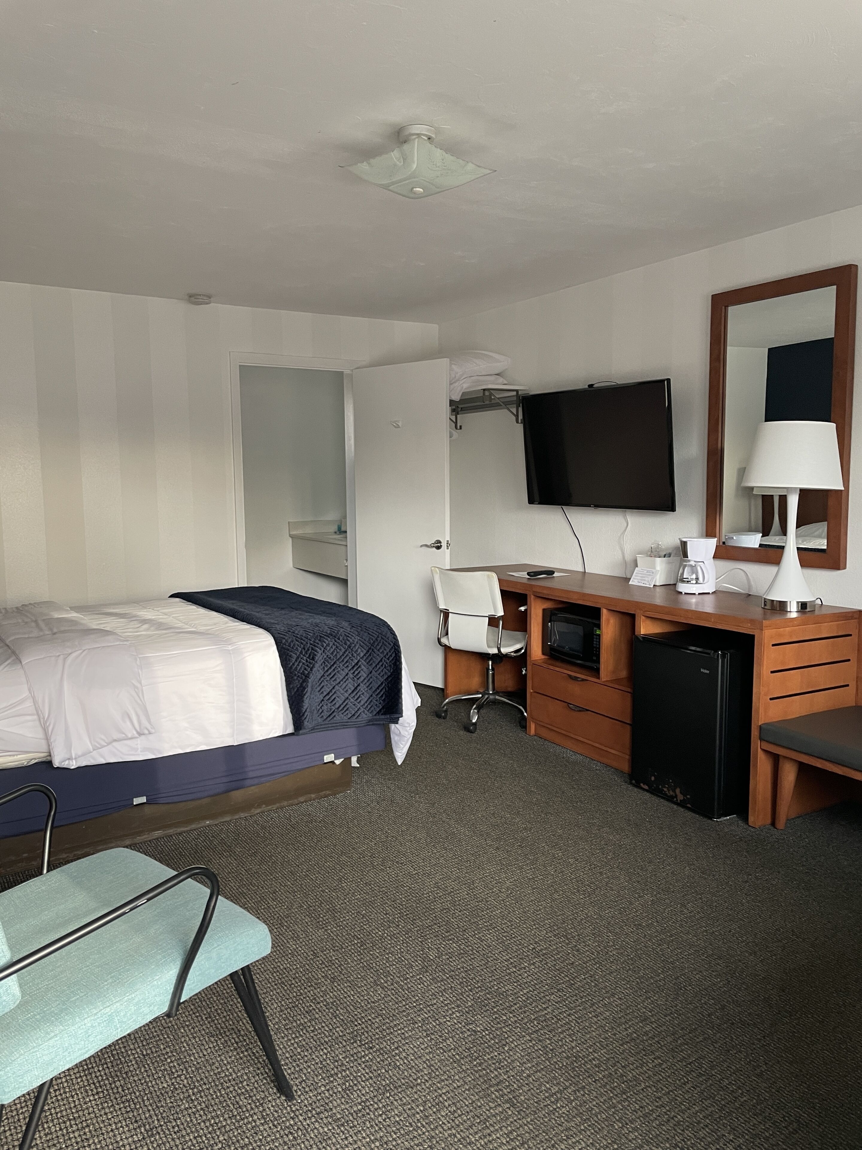 Une chambre d’hôtel équipée d’un lit, d’un bureau avec un ordinateur, d’une télévision, d’un miroir et d’un petit réfrigérateur.