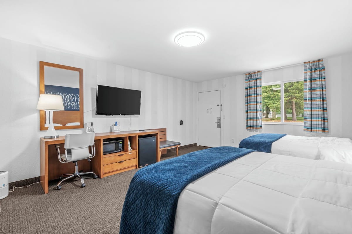 Une chambre d’hôtel avec deux lits, un bureau avec une chaise, une télévision et une fenêtre avec des rideaux.