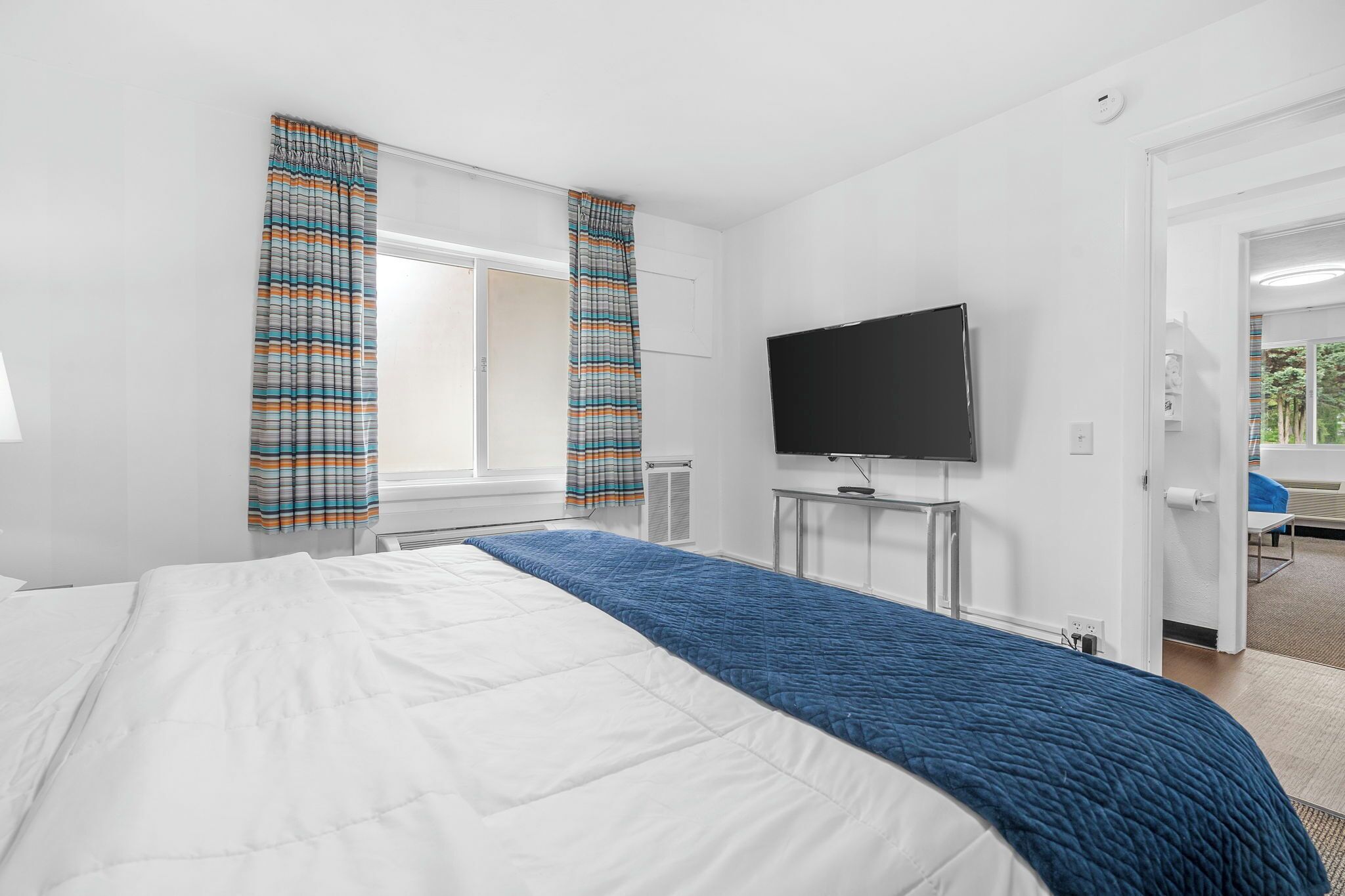 A hotel room with a bed, a TV, and a window with curtains.