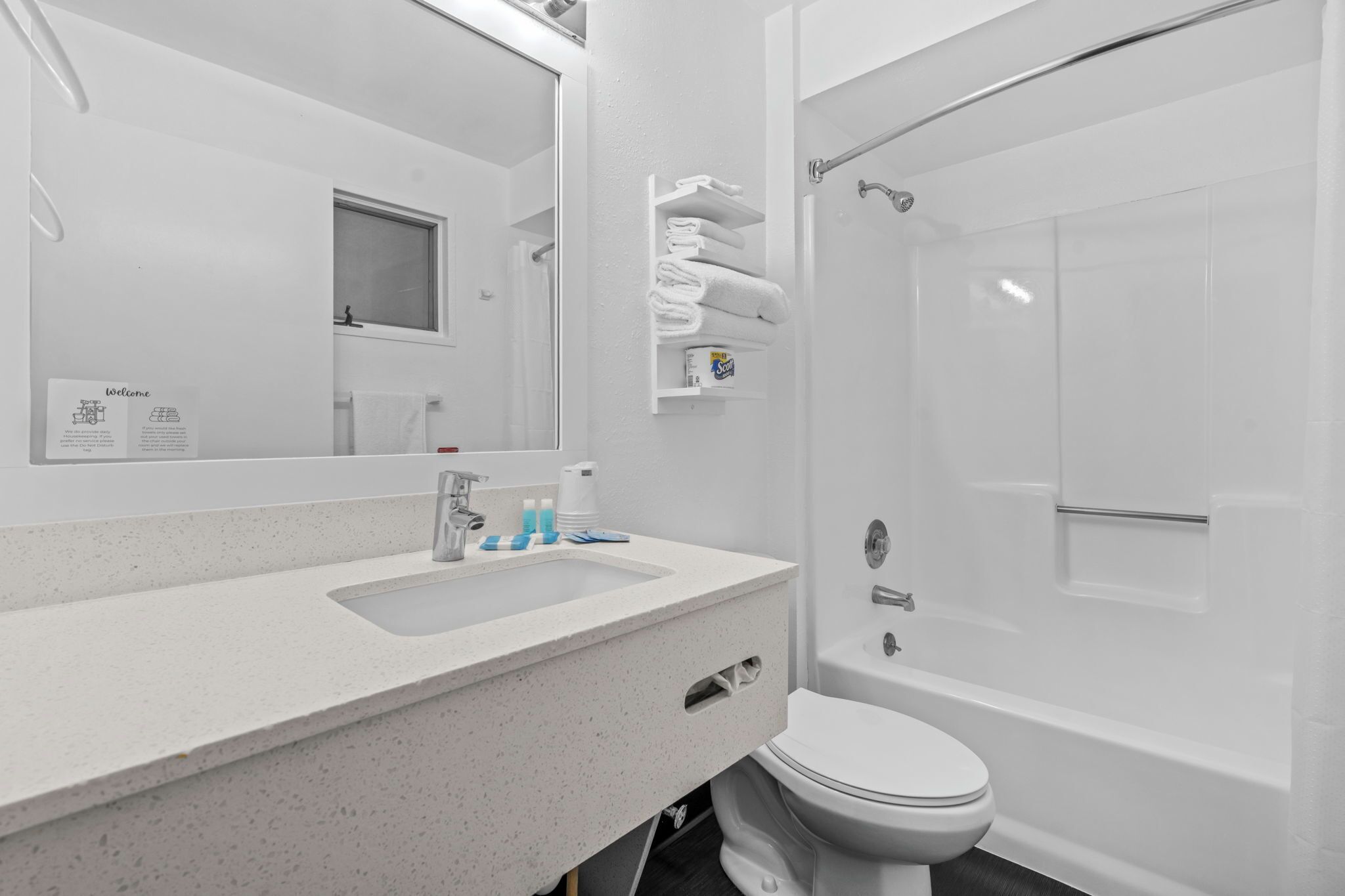 Une salle de bain moderne avec un lavabo, des toilettes et une baignoire, tous de couleur blanche. On y trouve un porte-serviettes avec des serviettes pliées et une étagère contenant des articles de toilette.