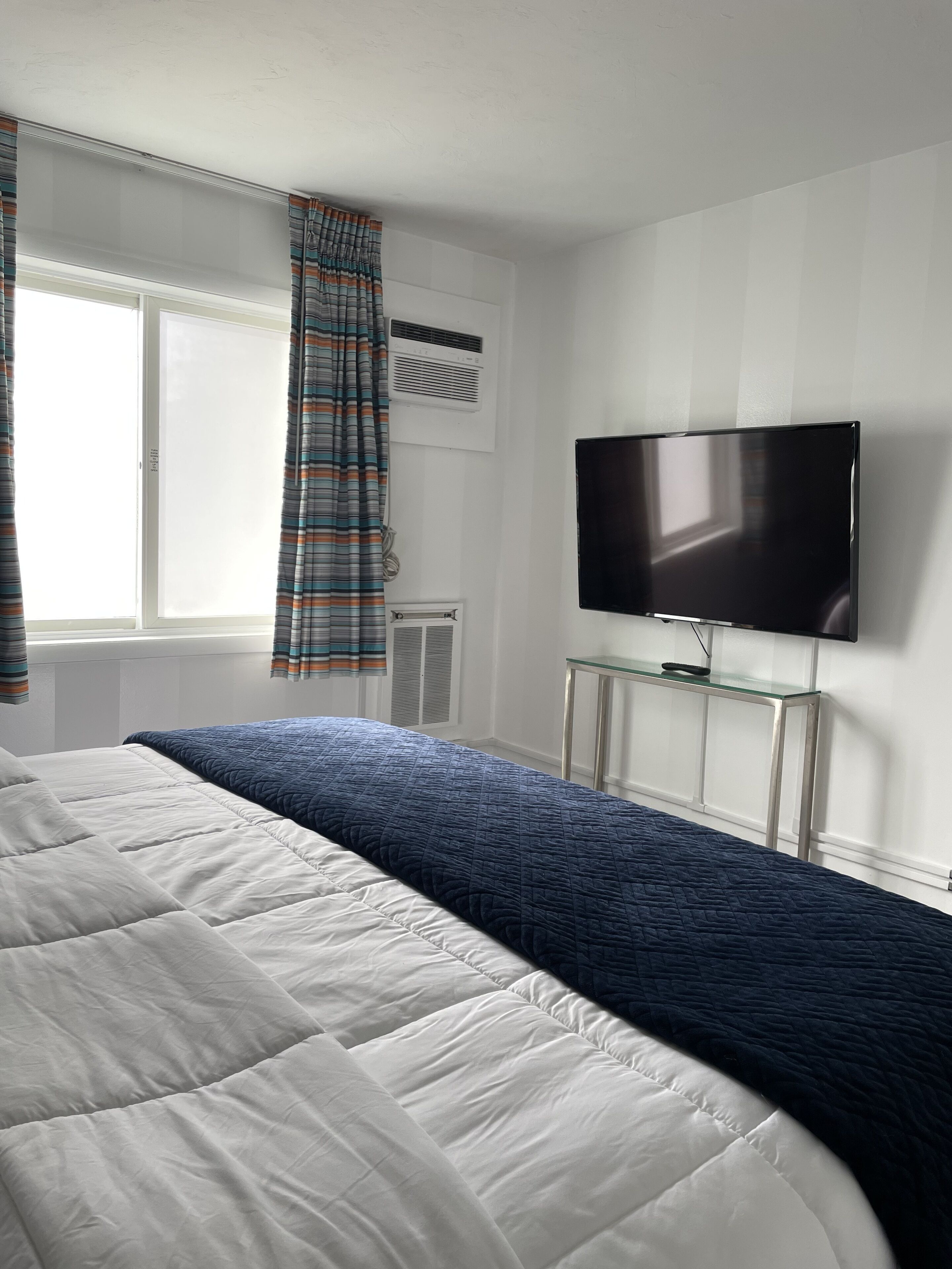 A bedroom with a large bed, a flat-screen TV mounted on the wall, and an air conditioning unit.