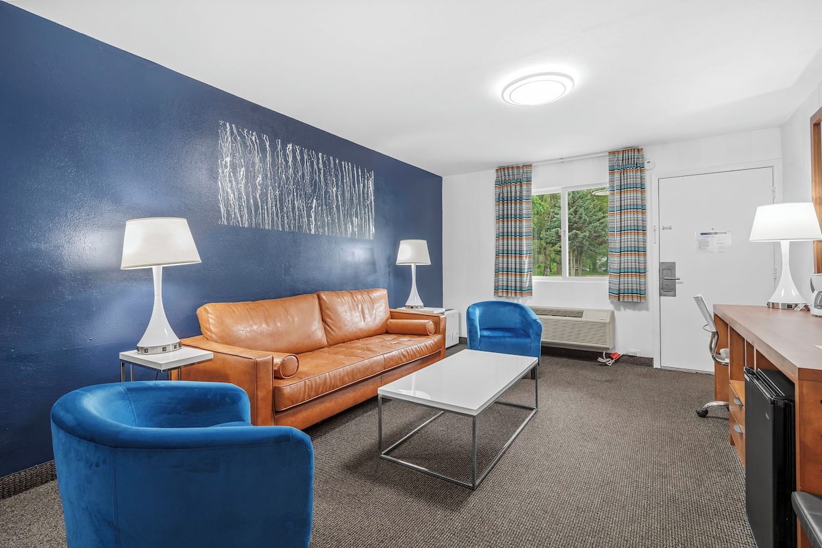 Une pièce moderne avec un mur d’accent bleu, un canapé en cuir marron, des fauteuils bleus, une table basse blanche et un coin cuisine.