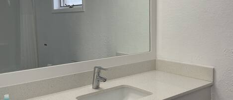 A bathroom with a white sink, a mirror, and a window.