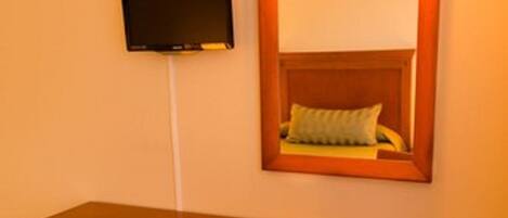 Un bureau en bois avec une chaise, un téléviseur fixé au mur et un miroir avec un luminaire placé au-dessus.
