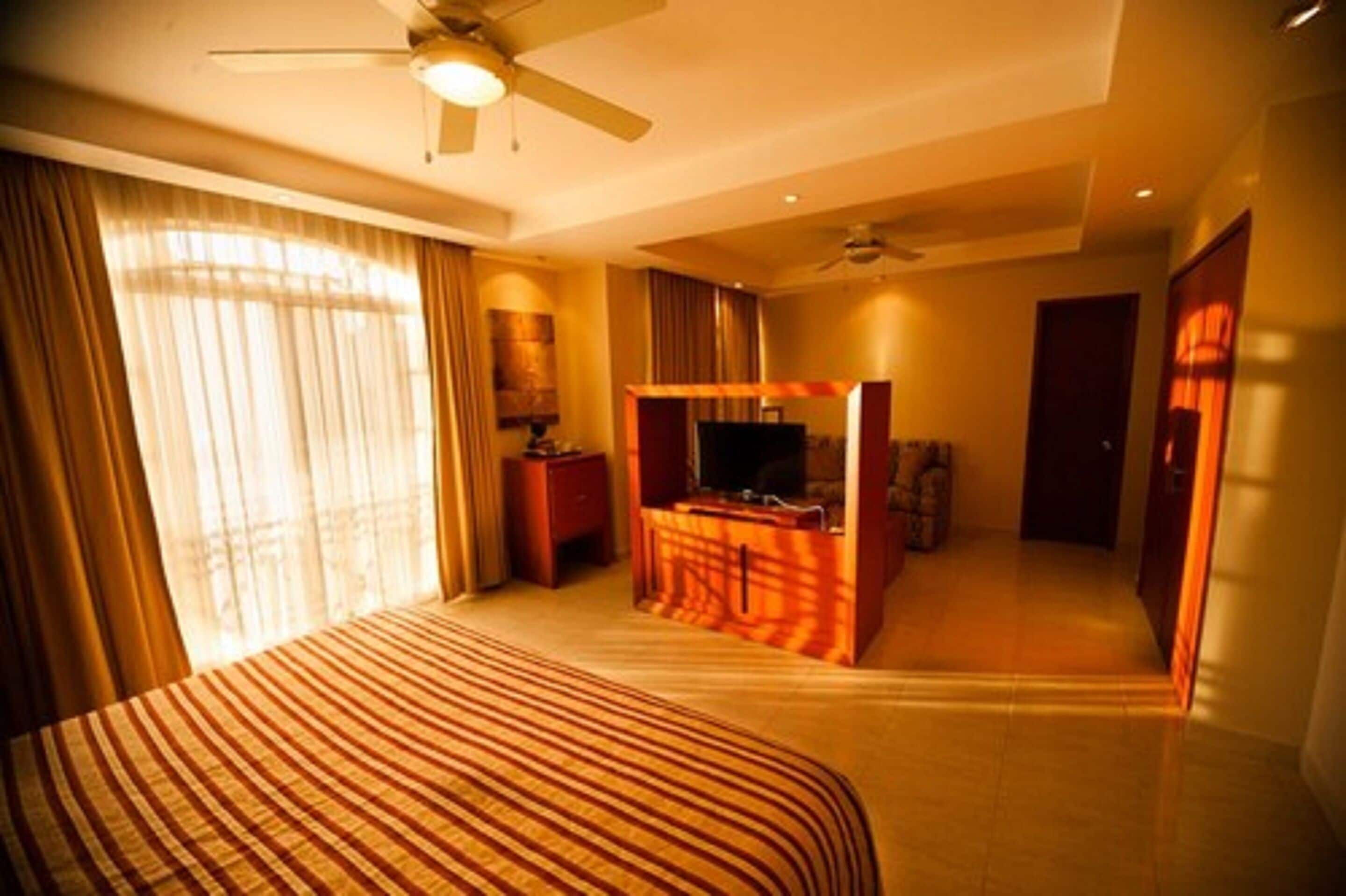 A hotel room with a bed, a desk, a television, and a ceiling fan.