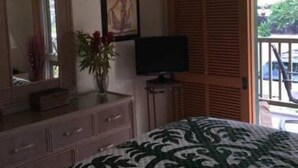 Een slaapkamer met een bed, een dressoir, een televisie, een plafondventilator, een raam en een deur die uitkomt op een buitenruimte.