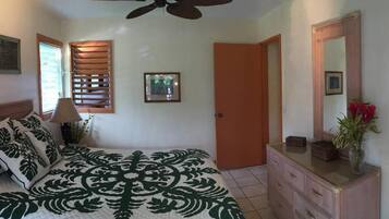 Un dormitorio con cama, ventilador de techo, cómoda, espejo y puerta.