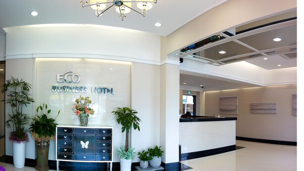 A reception area with a modern design, featuring a reception desk, potted plants, and a sign that reads "ECO BUSINESS HOTEL". - Eco Hotel (Pohang)