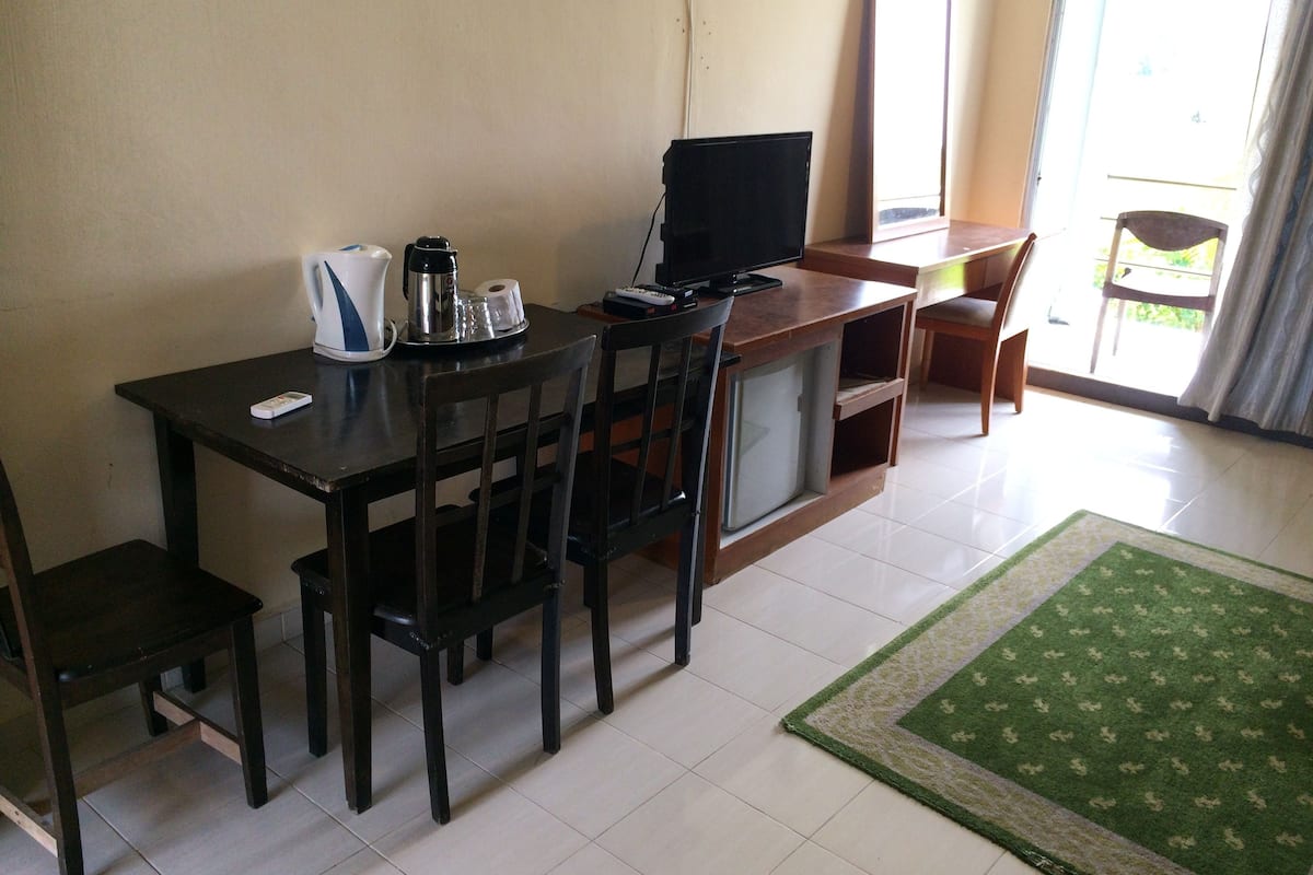 A small, well-lit room with a wooden desk, two chairs, a television, and a coffee maker.