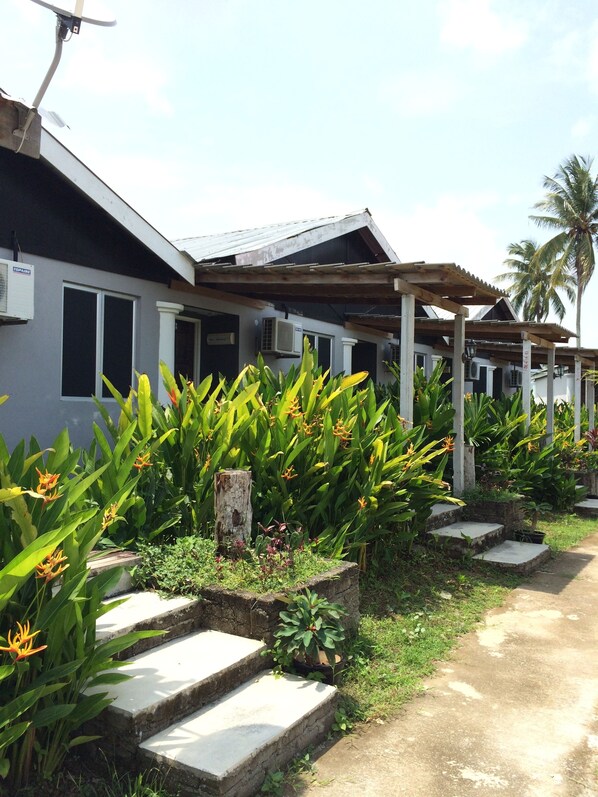 A row of single-story buildings with attached air conditioning units, surrounded by lush tropical plants and a palm tree. - Pondok Muara Chalet (Langkawi)
