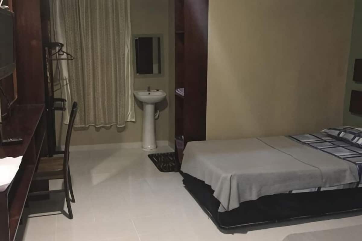 A bedroom with a bed, a sink, a chair, and a window.