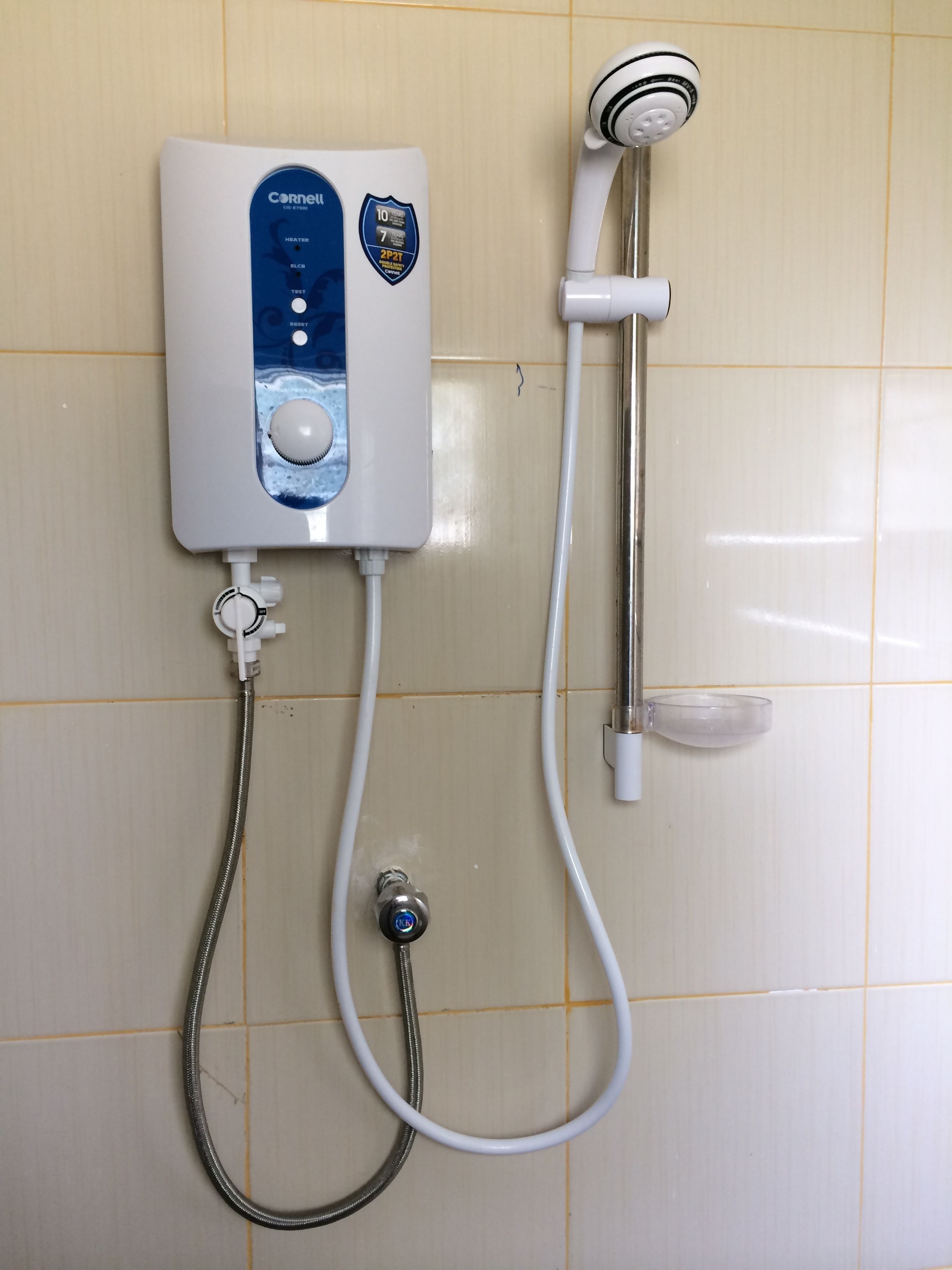 Een badkamer met een witte betegelde muur, een witte douchekop en een witte boiler met bedieningspaneel.