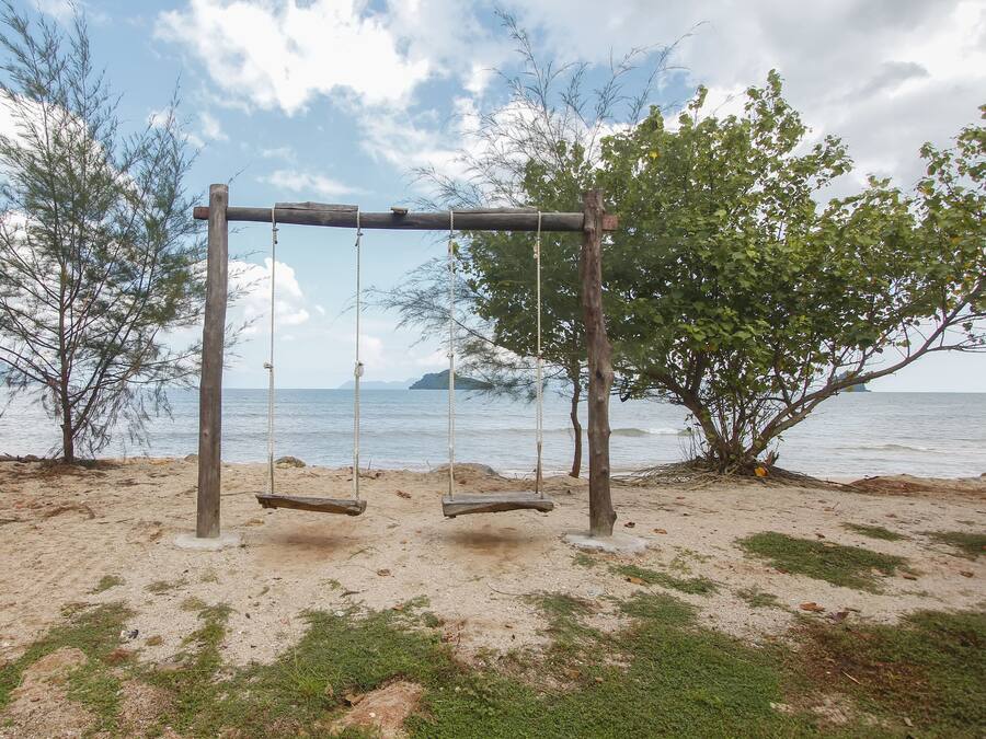 A beach with a wooden swing set and a tree in the background.