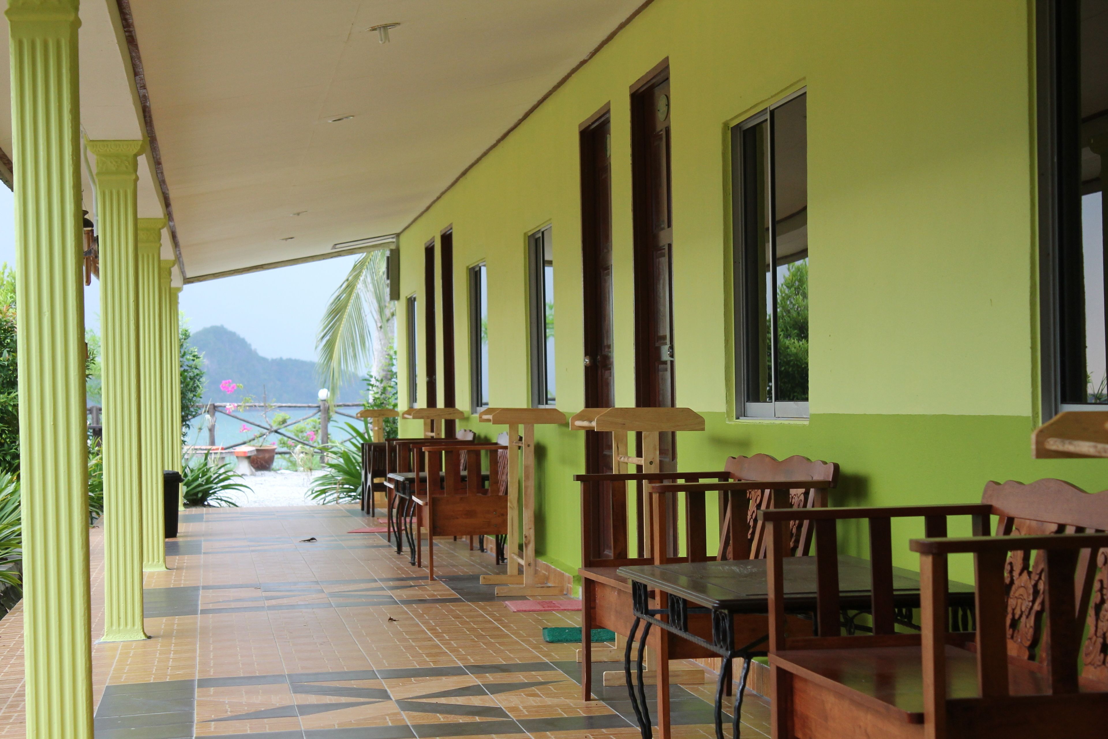 A covered outdoor seating area with wooden tables and chairs, green walls, and a tiled floor.