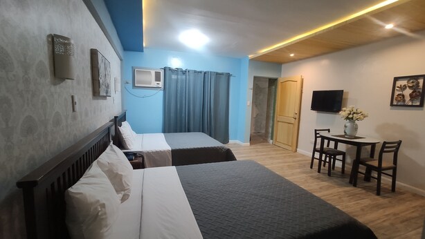 A hotel room with two beds, a desk with chairs, a TV, and a door leading to another room. - Nikita's Place Hotel (Calapan)