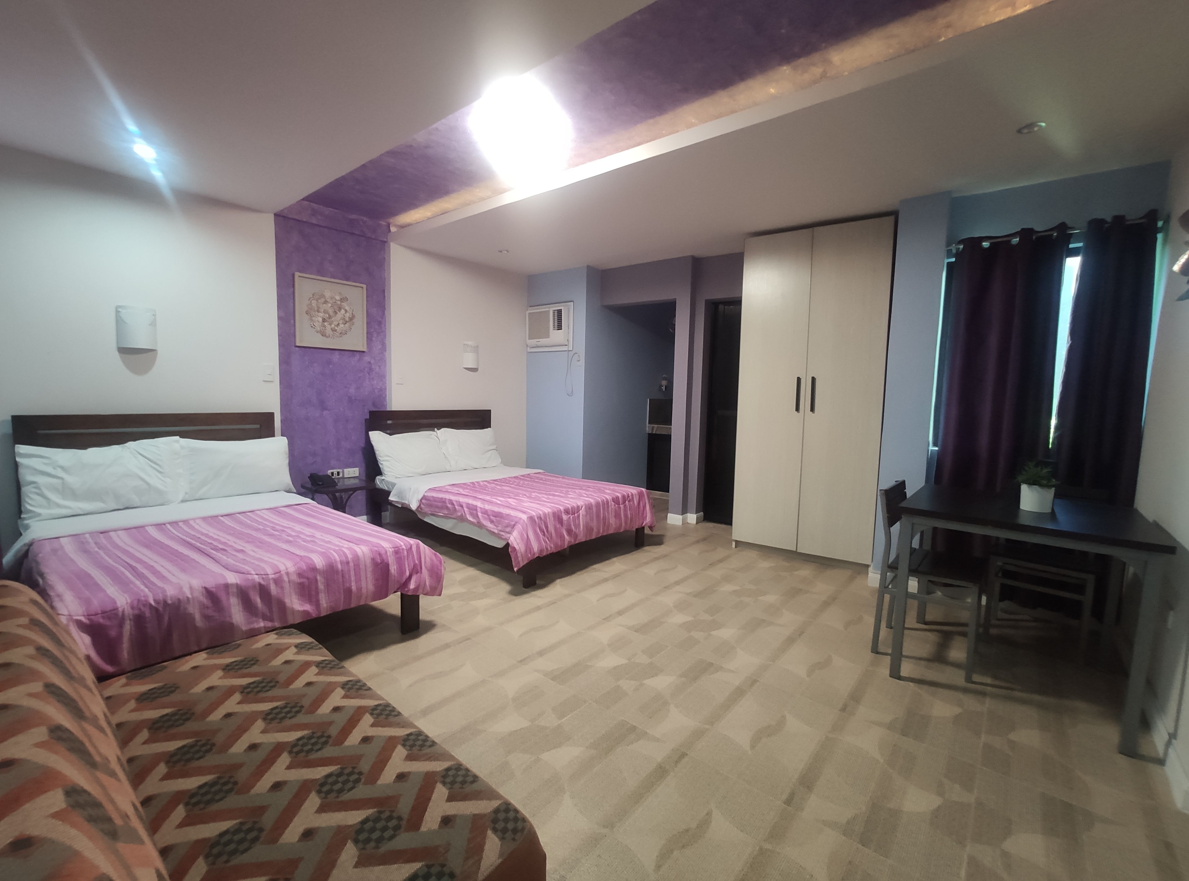 Habitación de hotel con dos camas, un escritorio, un armario y una pequeña mesa con una planta.