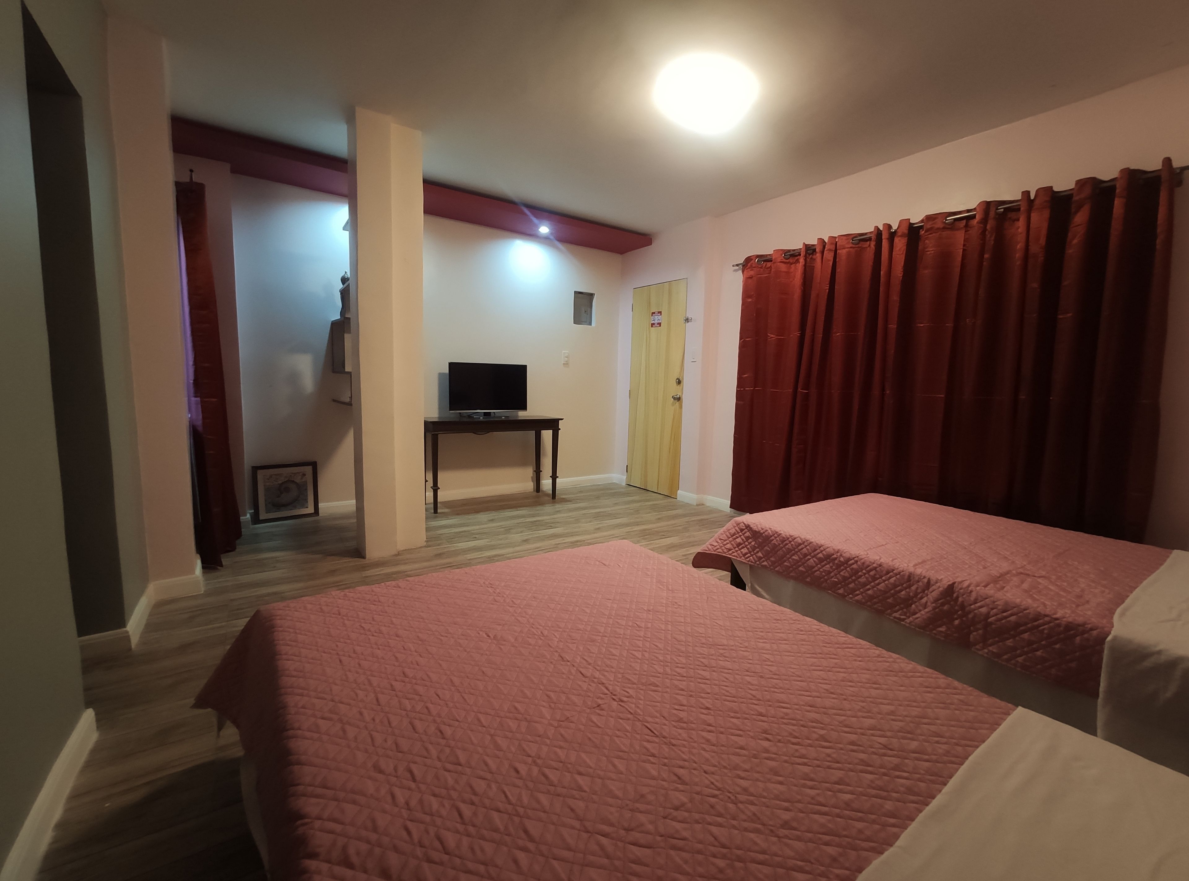 A room with two beds, a TV on a stand, a door, and red curtains.