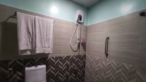 A bathroom with a toilet, a towel rack, a shower head, and a handrail. - Nikita's Place Hotel (Calapan)
